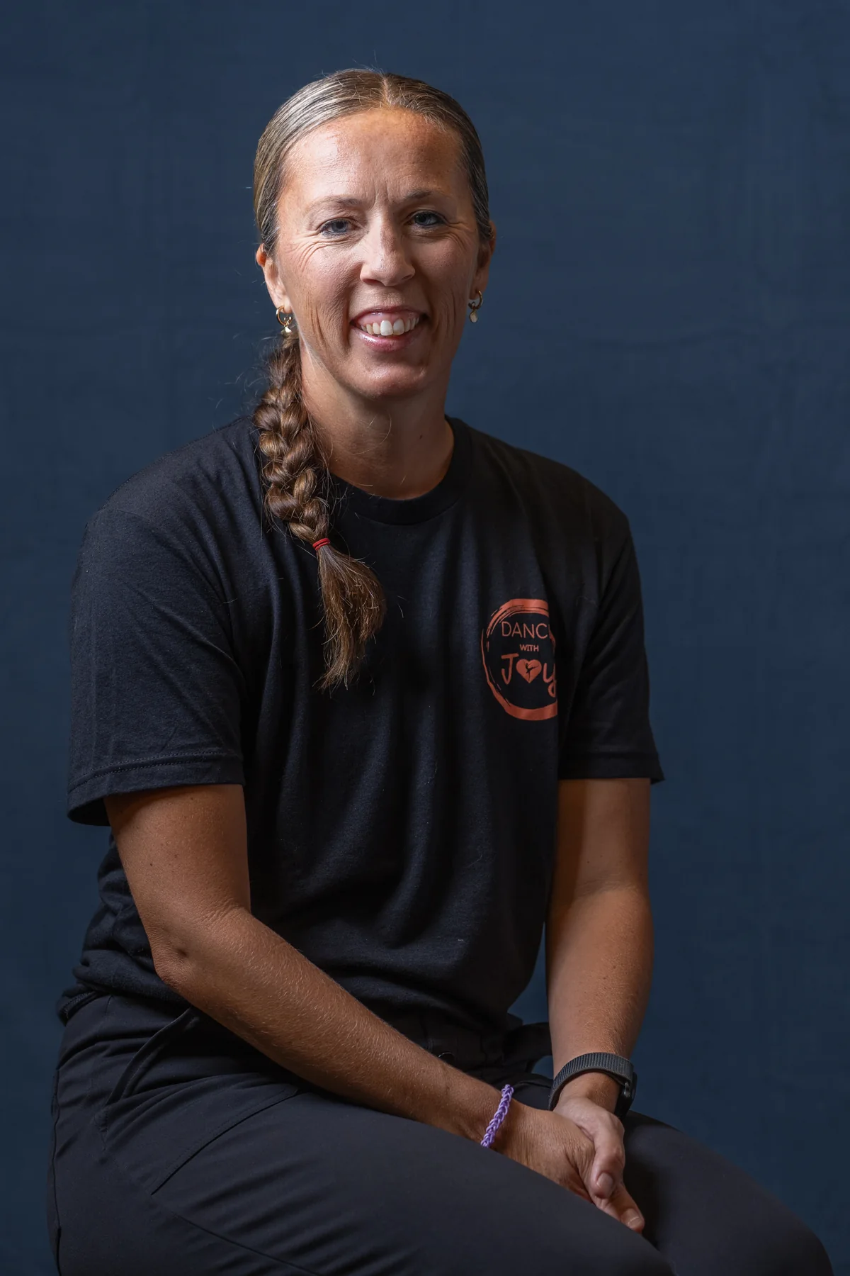 Dance with Joy team member seated against a dark studio backdrop